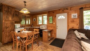 L'intérieur d'une cabane comprend une table à manger en bois, des chaises, un coin cuisine, un canapé et une porte avec une fenêtre.