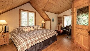 Une chambre confortable avec un grand lit, un plafond en bois et une porte ornée d’un panneau de verre décoré de motifs de feuilles.