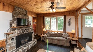 L’intérieur chaleureux d’un chalet avec une cheminée en pierre, un plafond en bois et un coin salon confortable.