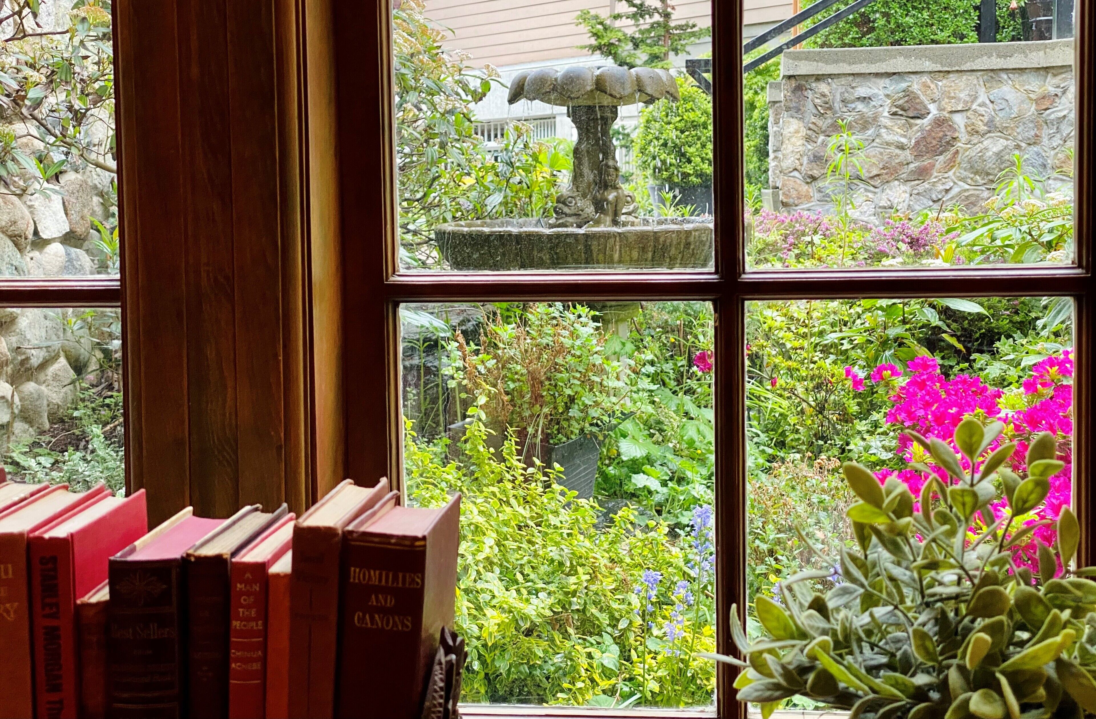 Una ventana con vistas a un jardín, un muro de piedra y una fuente.