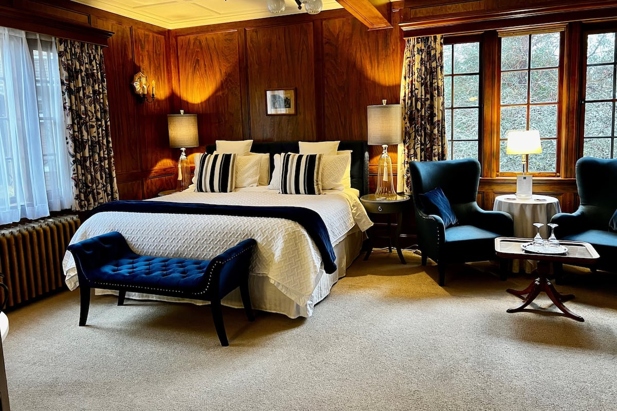 A well-appointed bedroom with a large bed, a sitting area with a chair and table, and a view through the window.