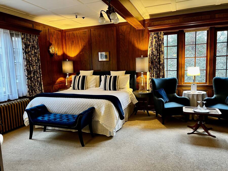Een smaakvol ingerichte slaapkamer met een groot bed, een zithoek met een stoel en een tafeltje, en uitzicht door het raam.