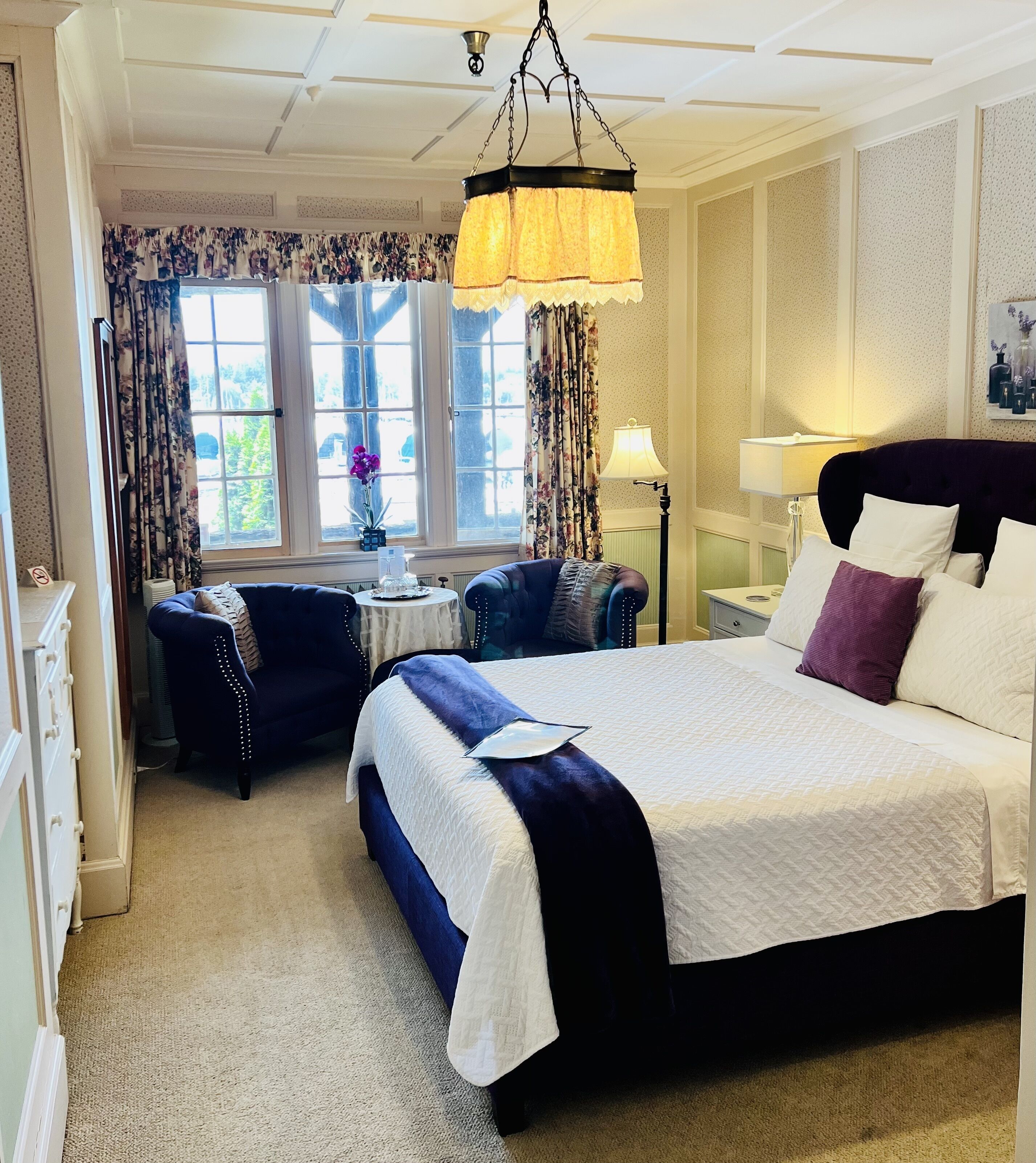 A hotel room with a large bed, two armchairs, a small table, and a window with curtains.