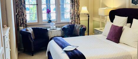 A hotel room with a large bed, two armchairs, a small table, and a window with curtains.