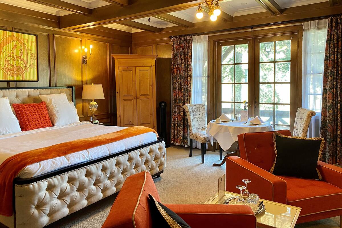 A hotel room with a large bed, a dining table with chairs, a wooden wardrobe, and a window with curtains.