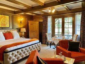 A hotel room with a large bed, a dining table with chairs, a wooden wardrobe, and a window with curtains.