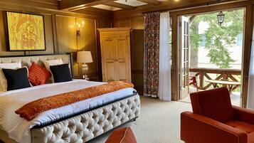 A hotel room with a large bed, a wooden wardrobe, a sitting area with a red chair, and a view of the outdoors through a glass door.