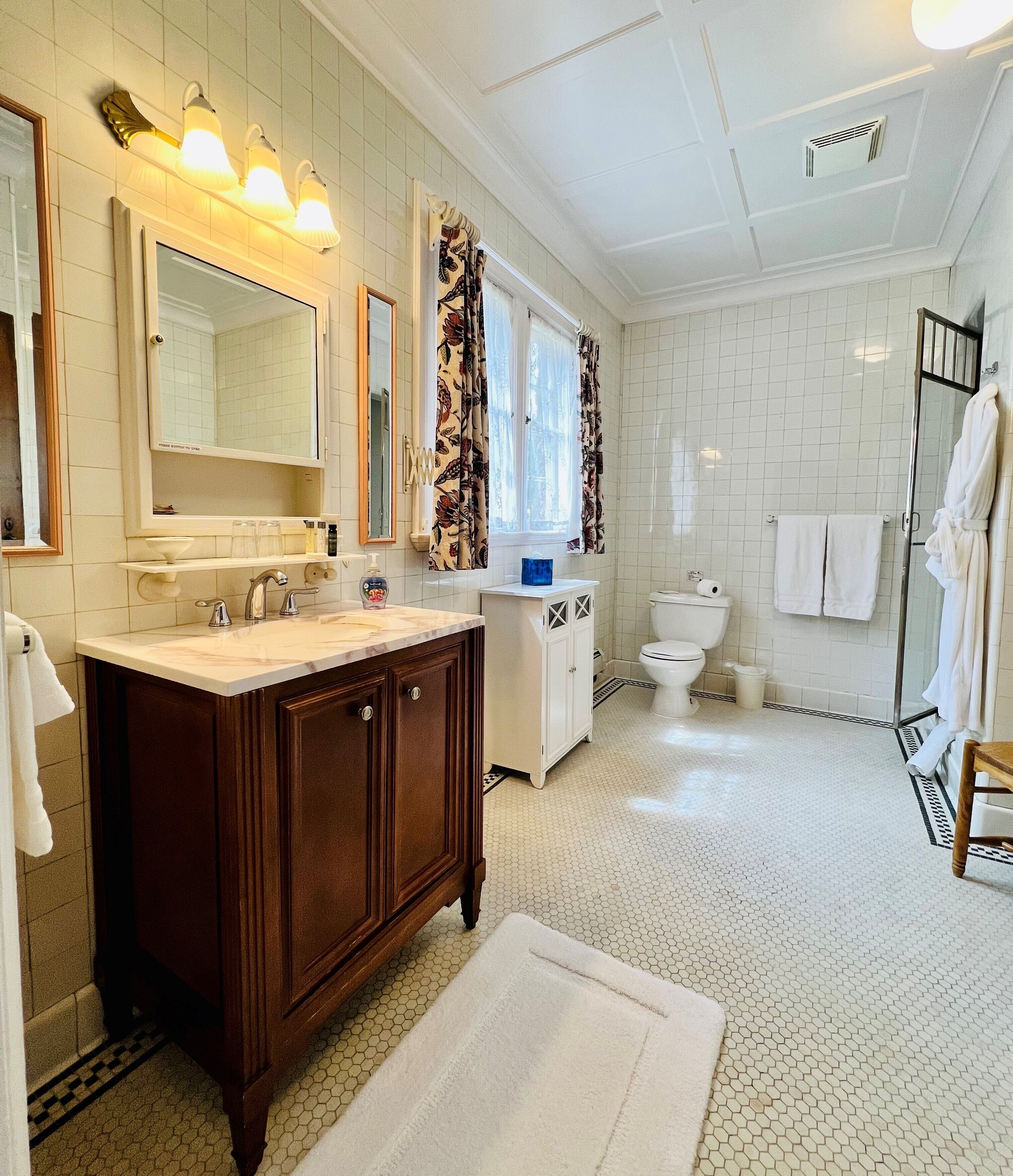 A bathroom with a wooden vanity, a large mirror, a sink, a toilet, and a shower area.