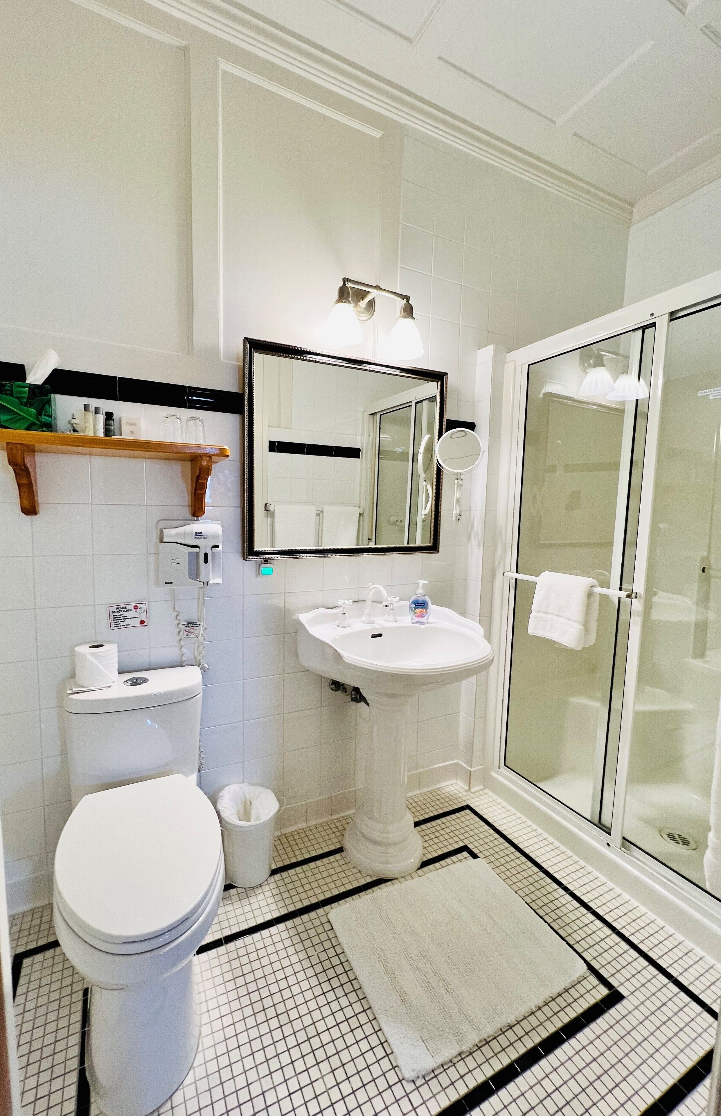 A bathroom with a toilet, sink, mirror, and glass shower enclosure.