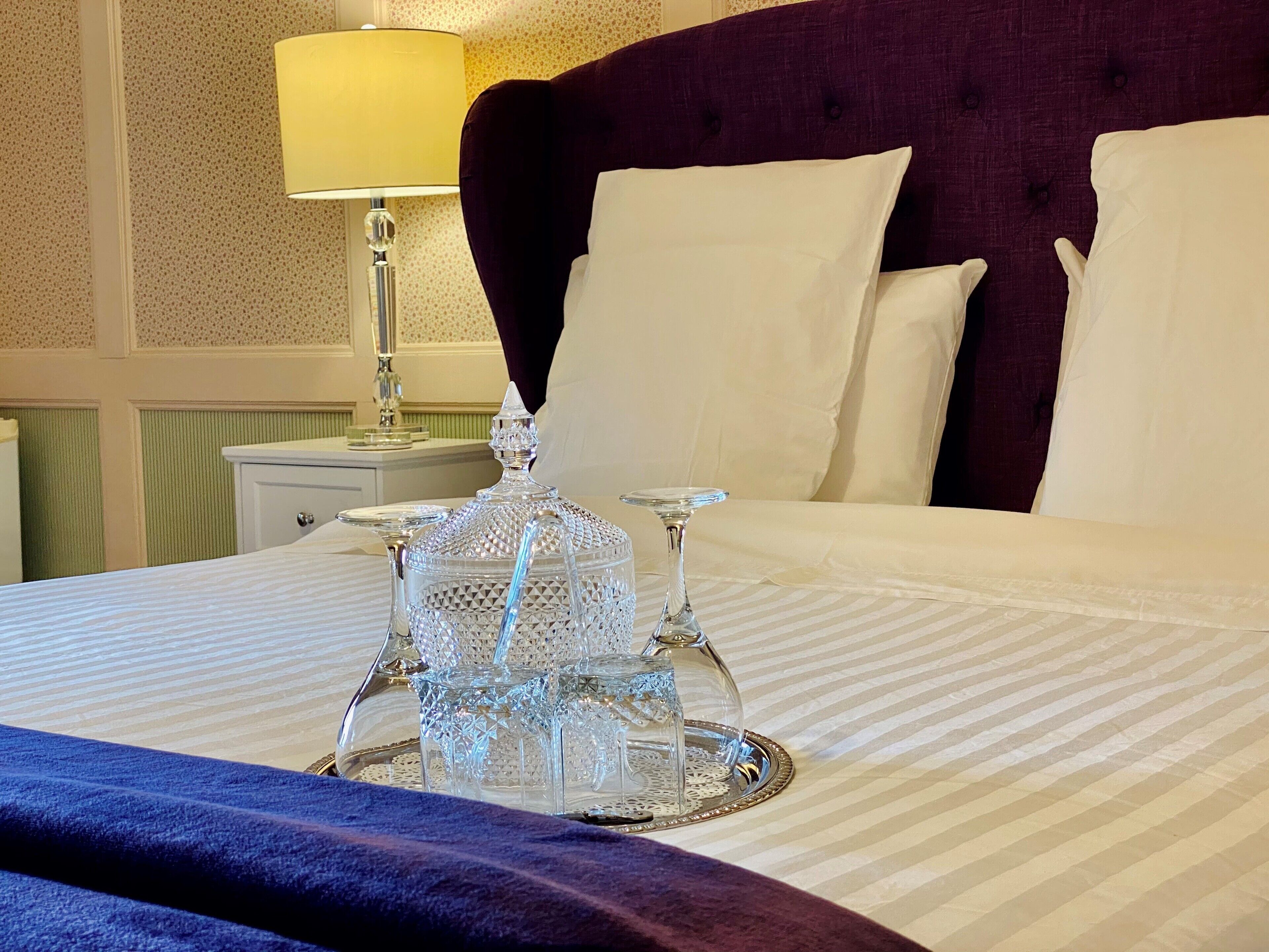 Un lit bien fait, avec une couvre-lit à rayures, un plateau décoratif en verre et une carafe en cristal posée sur le lit.