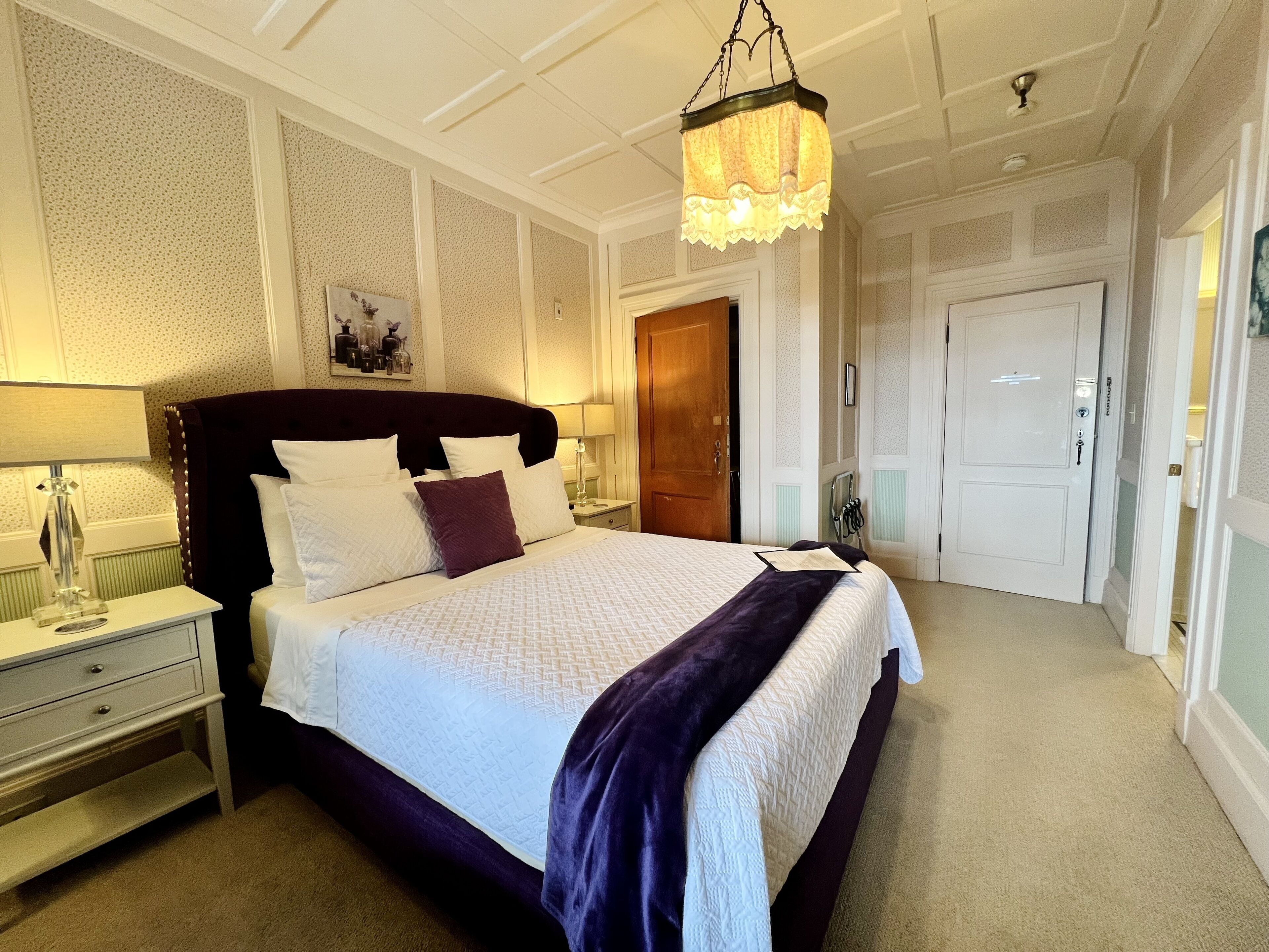 A neatly arranged bedroom with a large bed, a bedside table with a lamp, and a hanging light fixture.
