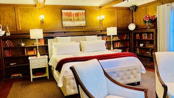 A spacious bedroom with a large bed, bedside tables, a reading chair, and a bookshelf filled with books.