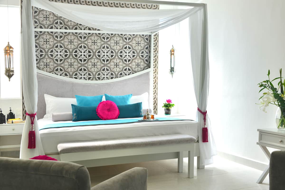 A four-poster bed with a patterned headboard, a bedside table with a lamp, and a potted plant on the nightstand.