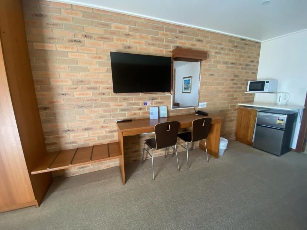 Ein Zimmer mit Backsteinwand, einem Flachbildfernseher über einem Holztisch mit zwei Stühlen, einer kleinen Kühlbox und einer Mikrowelle.