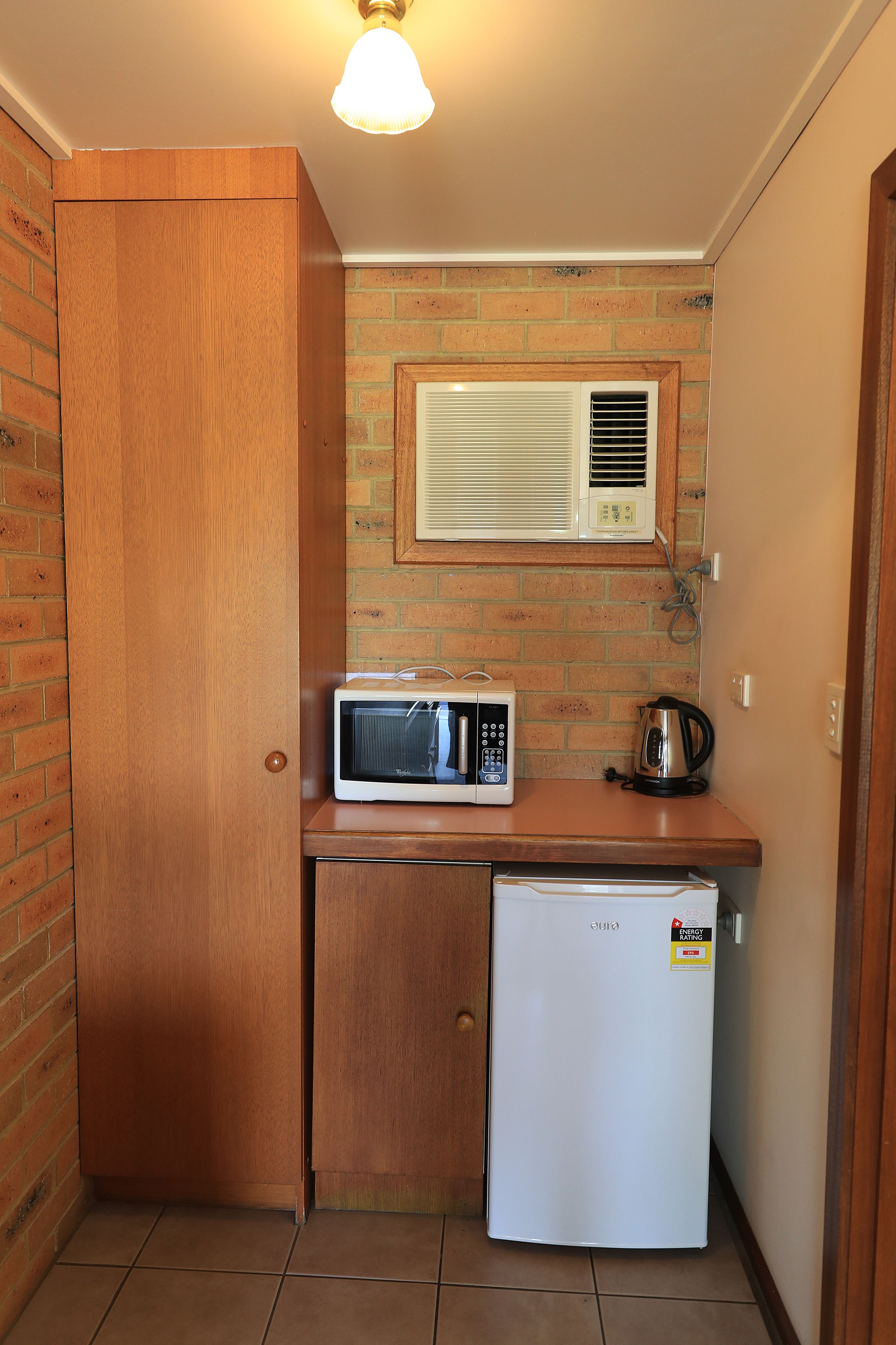 A compact kitchen with a microwave, a small refrigerator, and a kettle on a countertop.