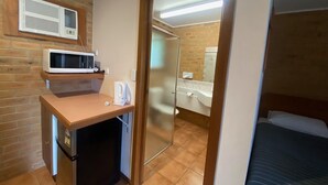 A compact room with a kitchenette, including a microwave, kettle, and refrigerator. A bathroom with a shower and sink is visible through an open door. - Quays Motel San Remo (San Remo)