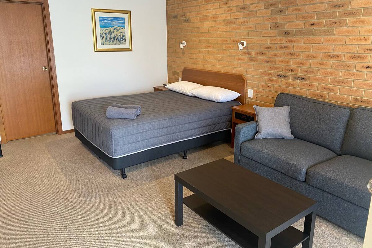 Une chambre avec un lit, un canapé, une table basse, un tableau et un mur en briques.