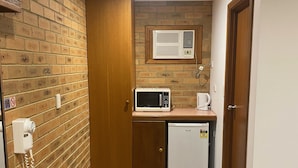 A compact kitchen with a microwave, a small refrigerator, and a built-in air conditioner. - Quays Motel San Remo (San Remo)