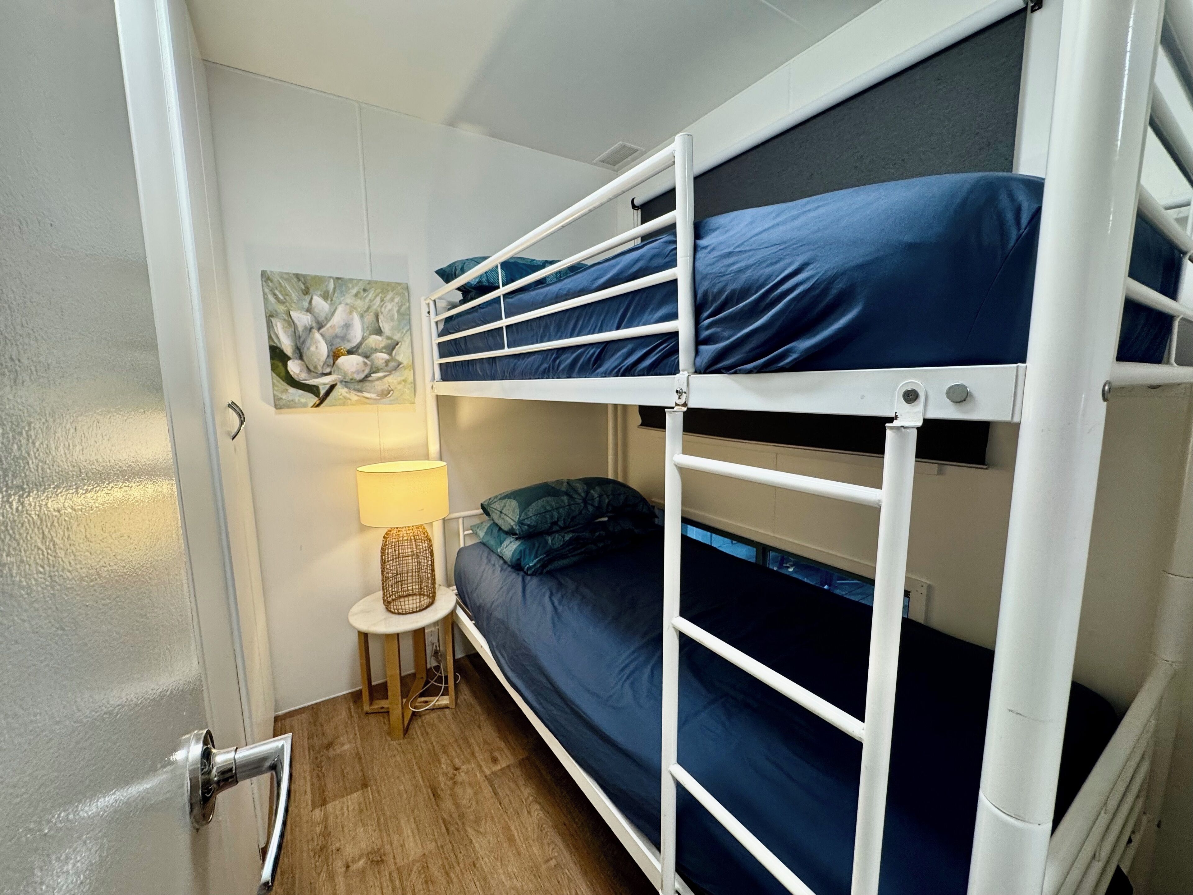 Une chambre avec un lit superposé, une petite table de chevet, une lampe et un tableau accroché au mur.