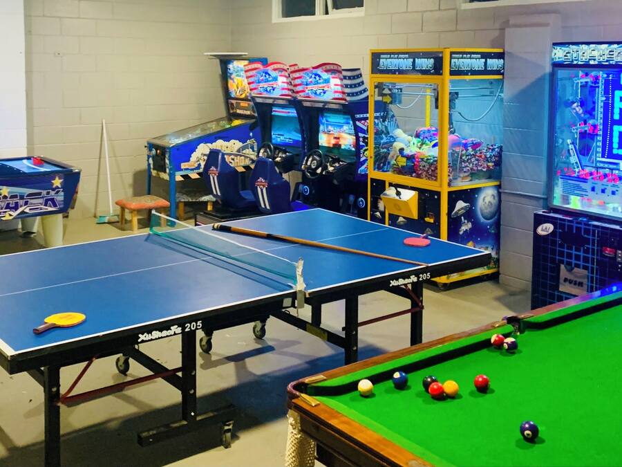 A recreational area with two ping pong tables, a pool table, and arcade games.