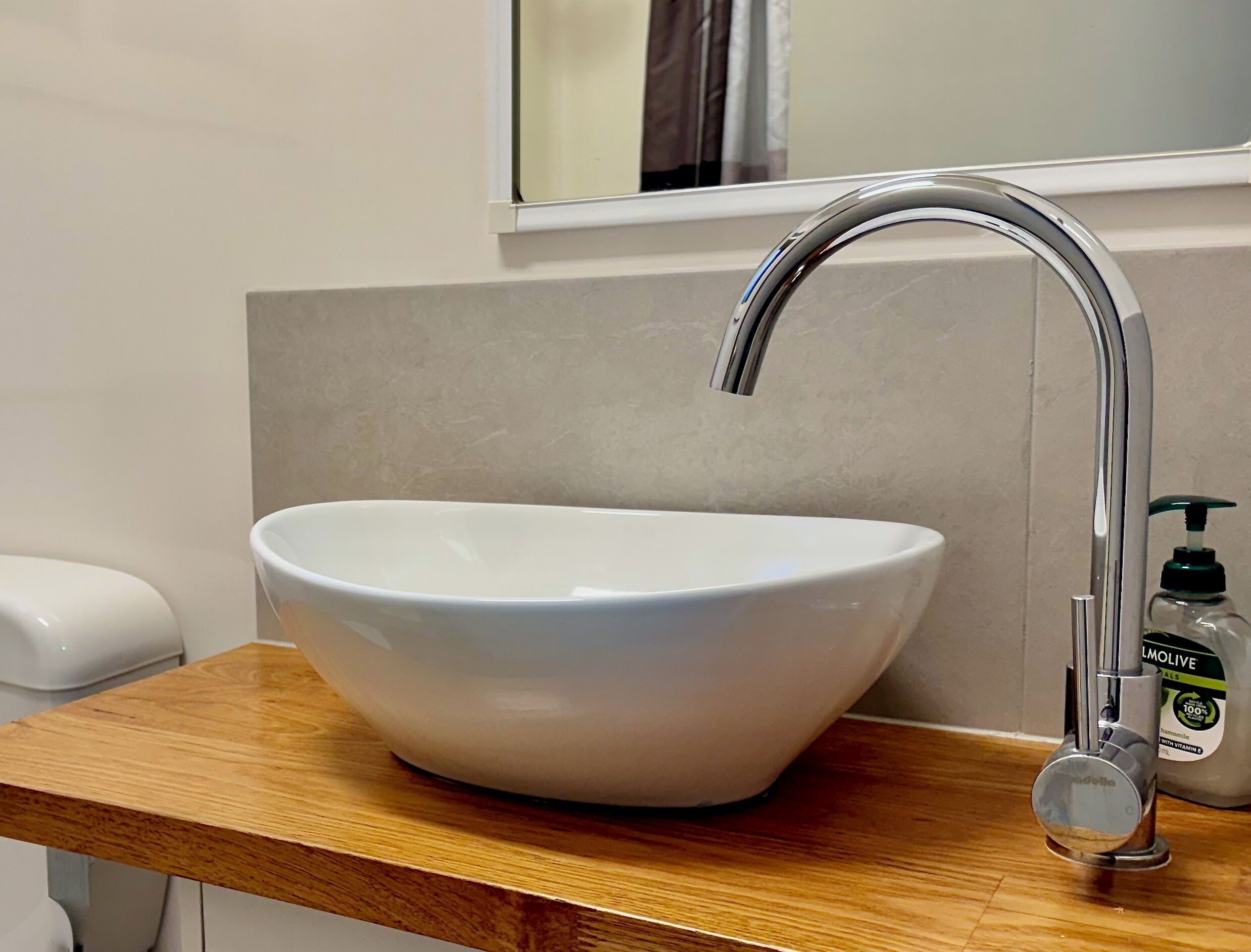 A white ceramic sink with a modern chrome faucet on a wooden countertop.