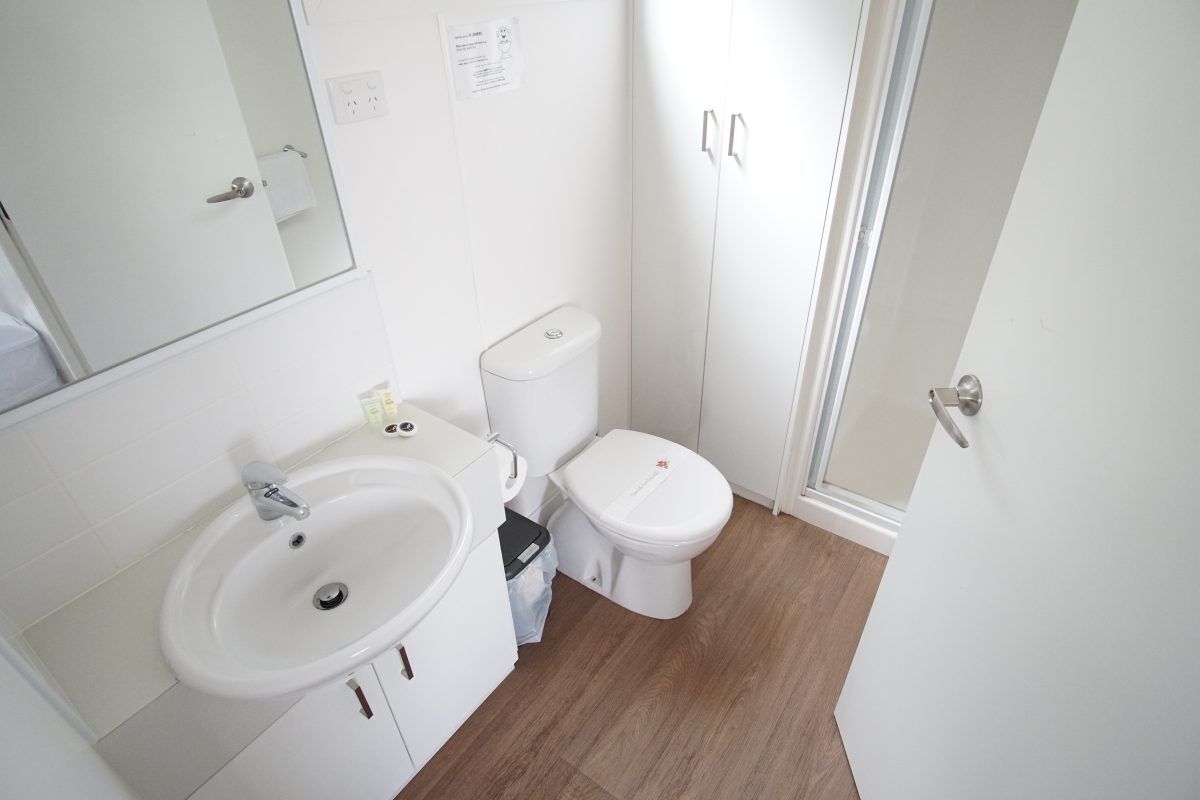 Une petite salle de bain propre, avec un lavabo, des toilettes et un miroir, le tout de couleur blanche.
