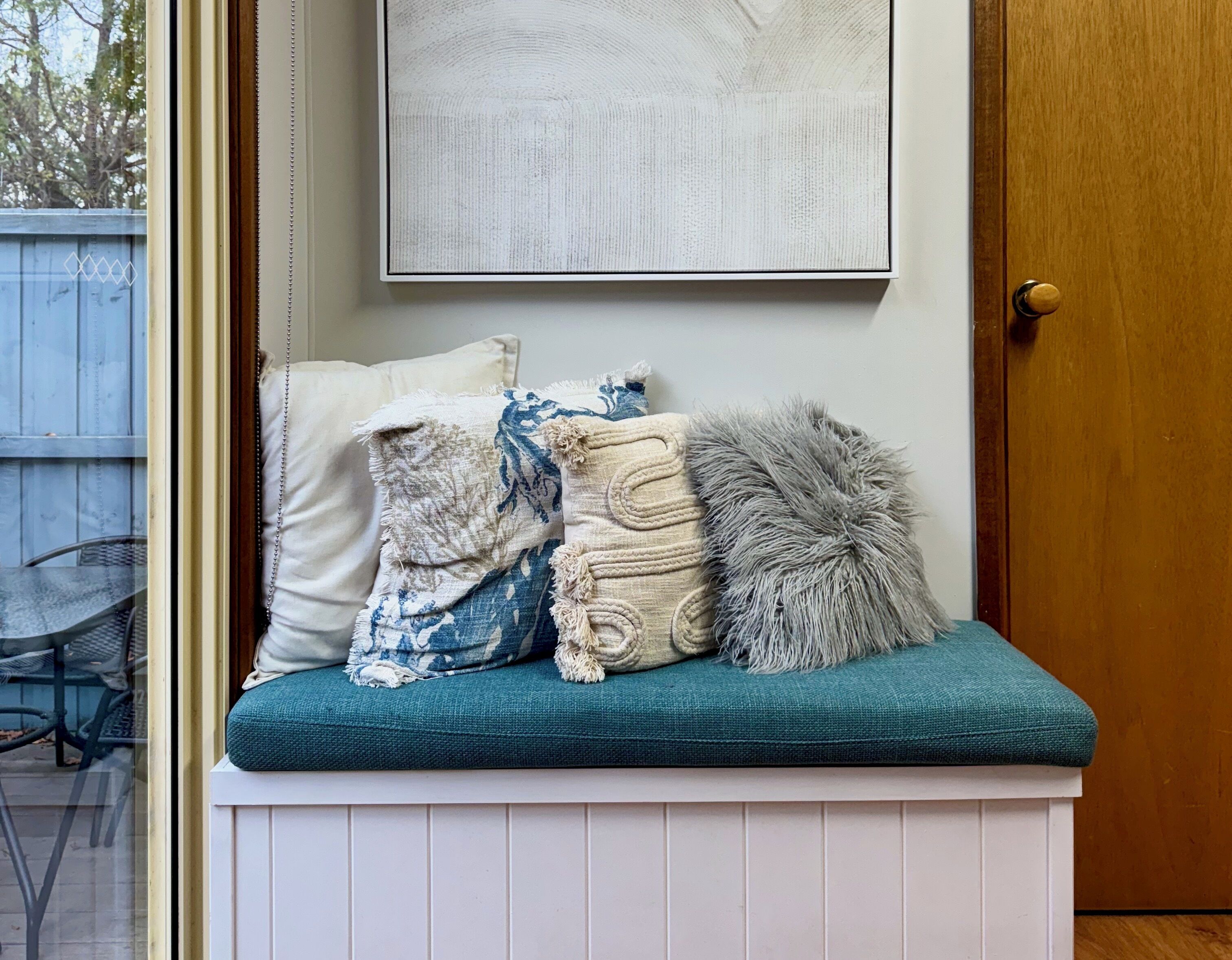A bench with cushions and a framed artwork above it.