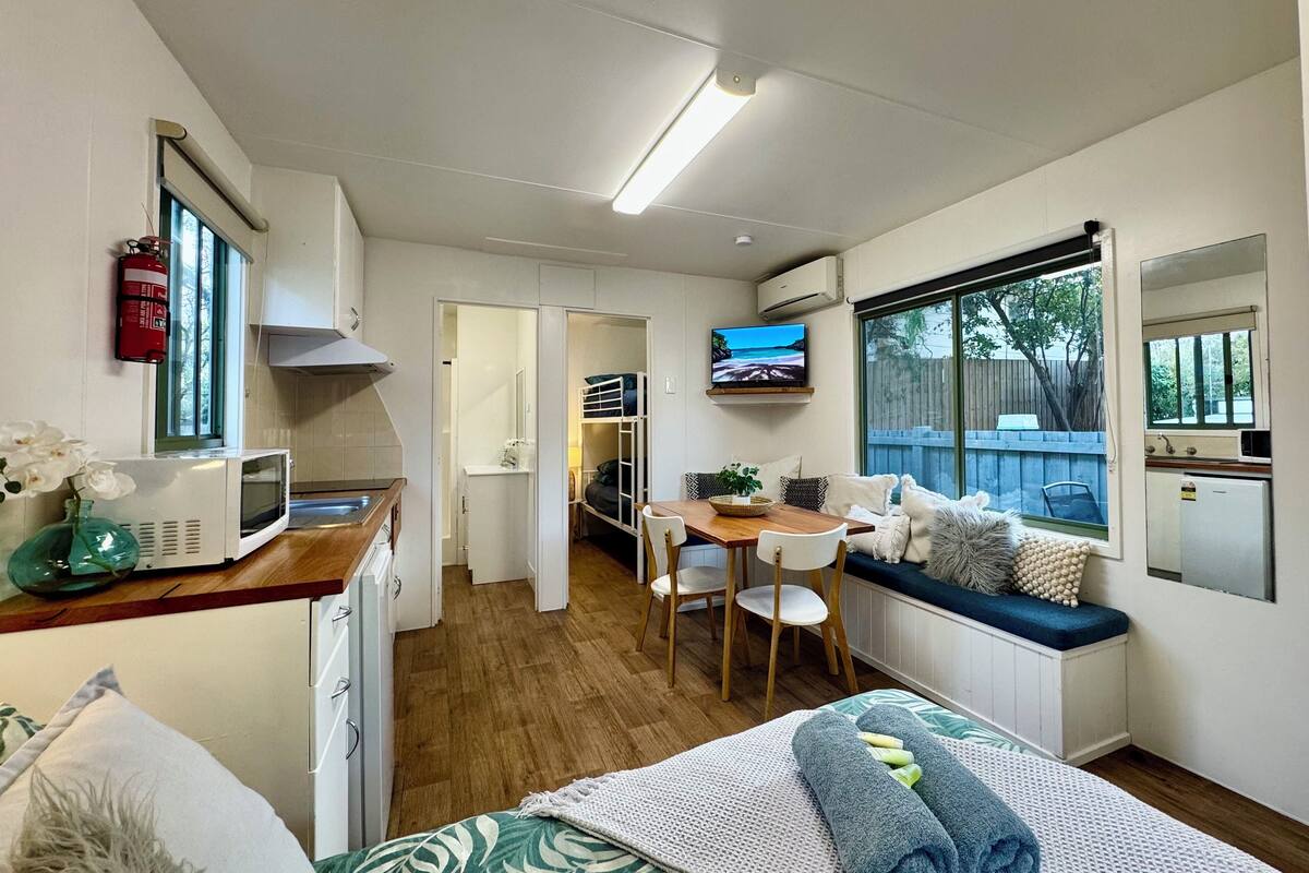 A compact room with a bed, a desk, a chair, a small kitchenette, a television, and a window with a view of the outdoors.