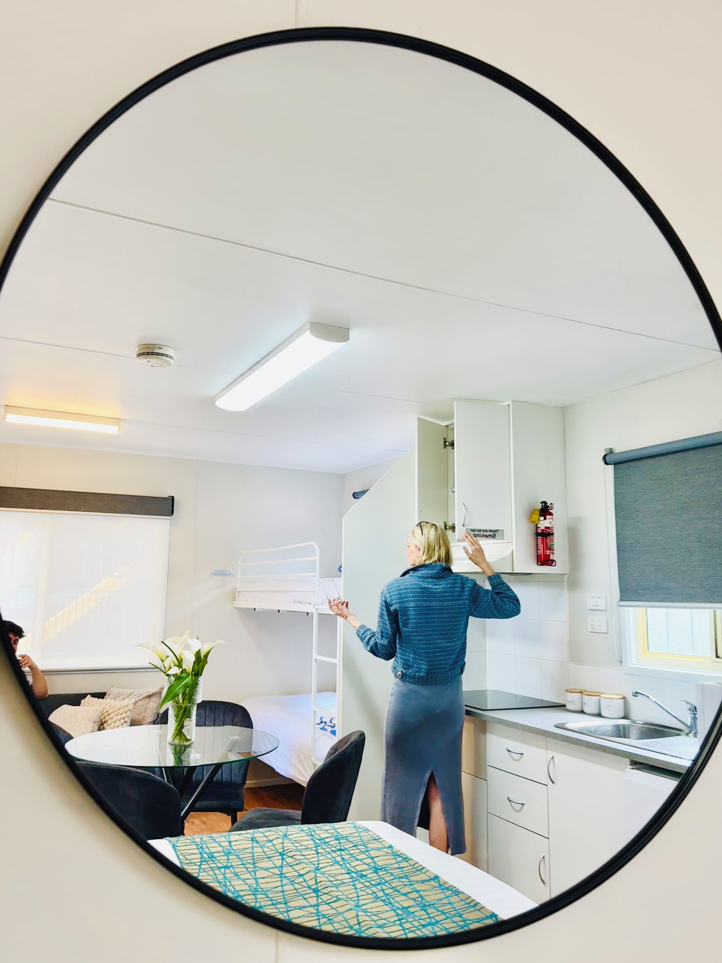 A modern, compact living space with a bunk bed, a dining area with a glass table, and a kitchenette with a sink and cabinets.
