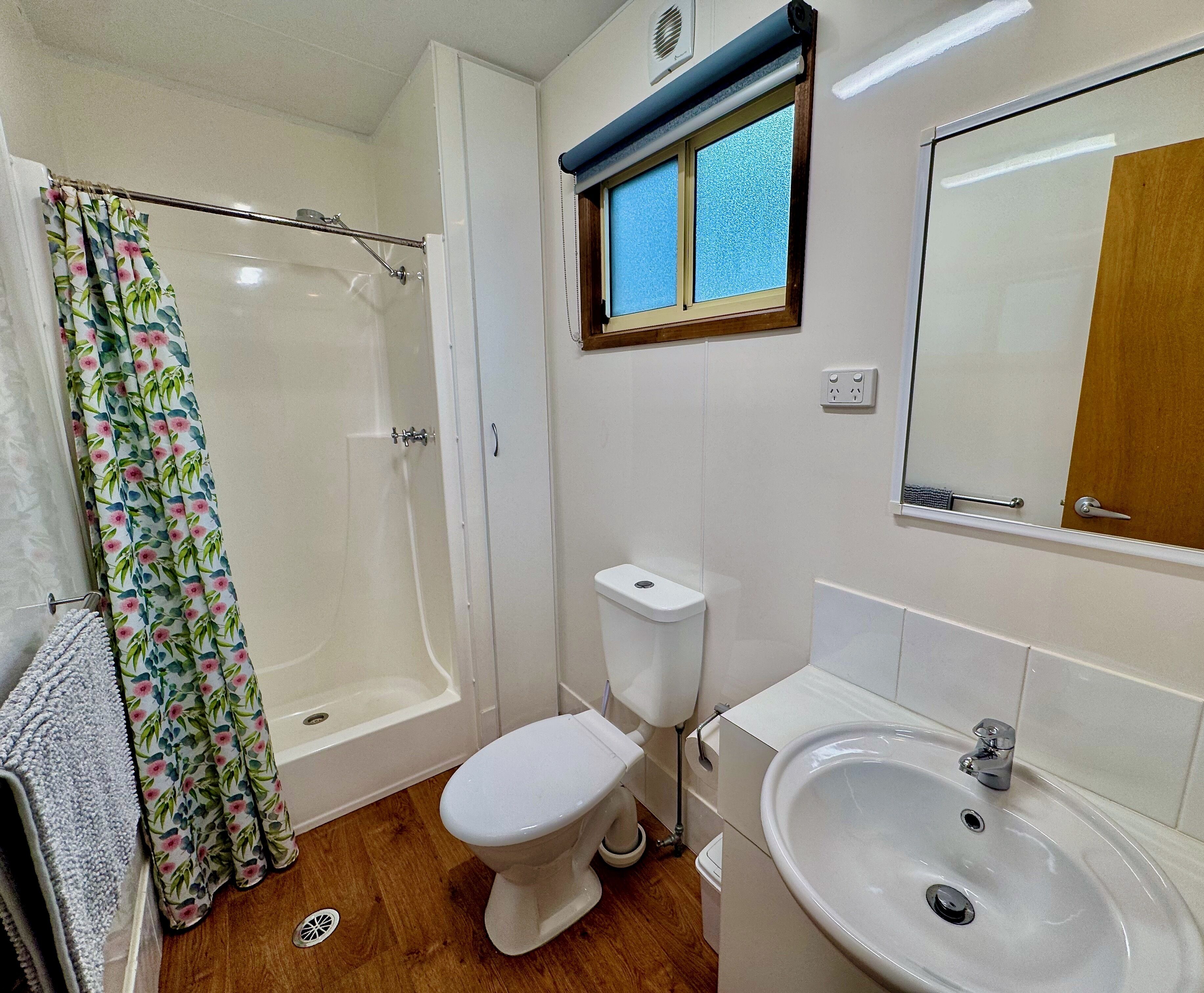 Ein Badezimmer mit Dusche, Toilette, Waschbecken und einem Fenster mit Jalousien.