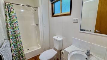 Un bagno con doccia, WC, lavandino e una finestra con persiane.