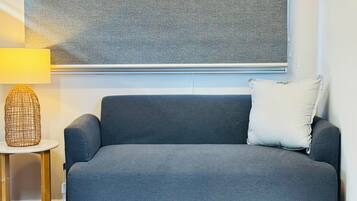 A grey sofa with a white pillow, a small round table with a lamp, and a textured wall.