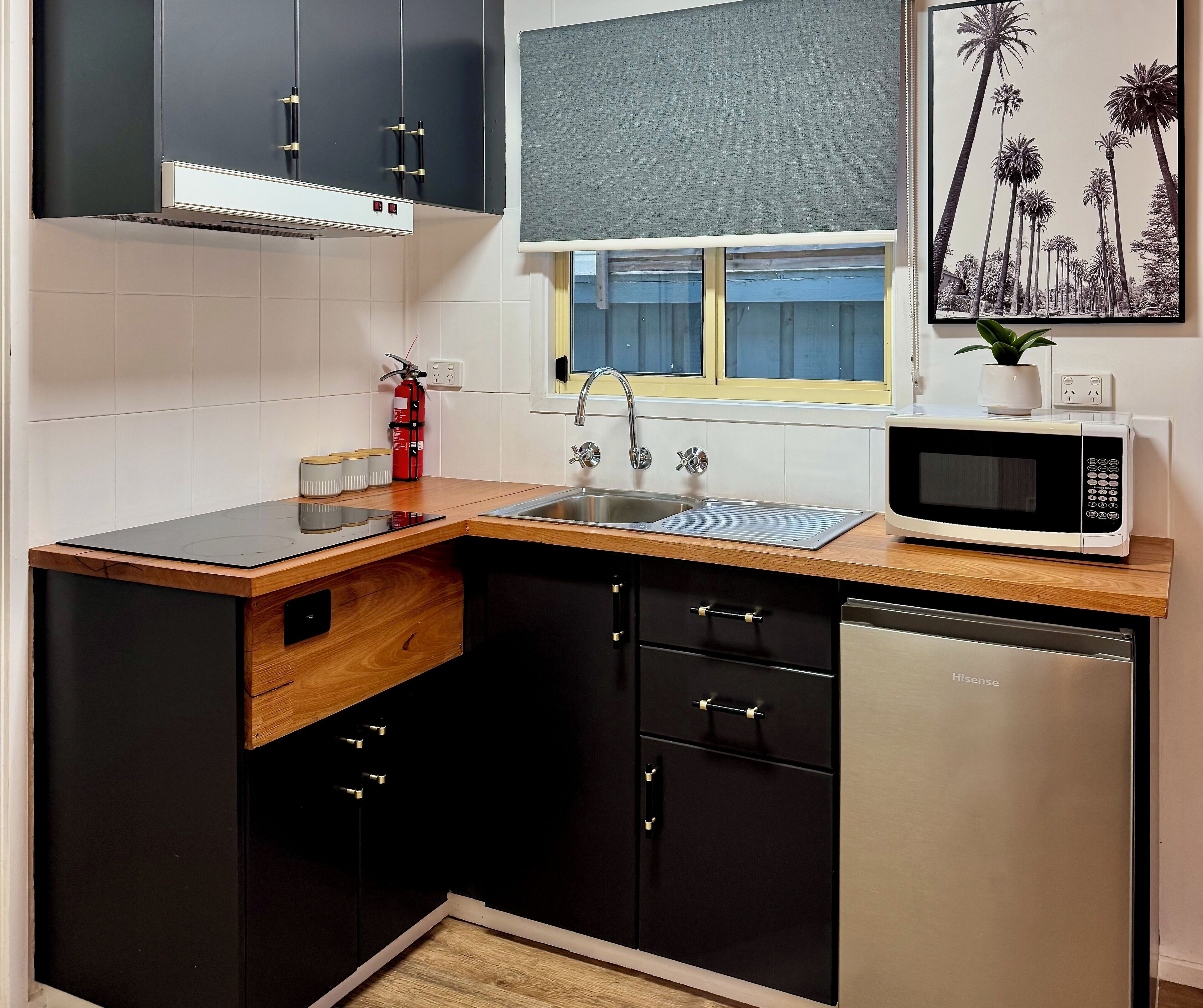 A compact kitchen with a wooden countertop, stainless steel appliances, and black cabinets.