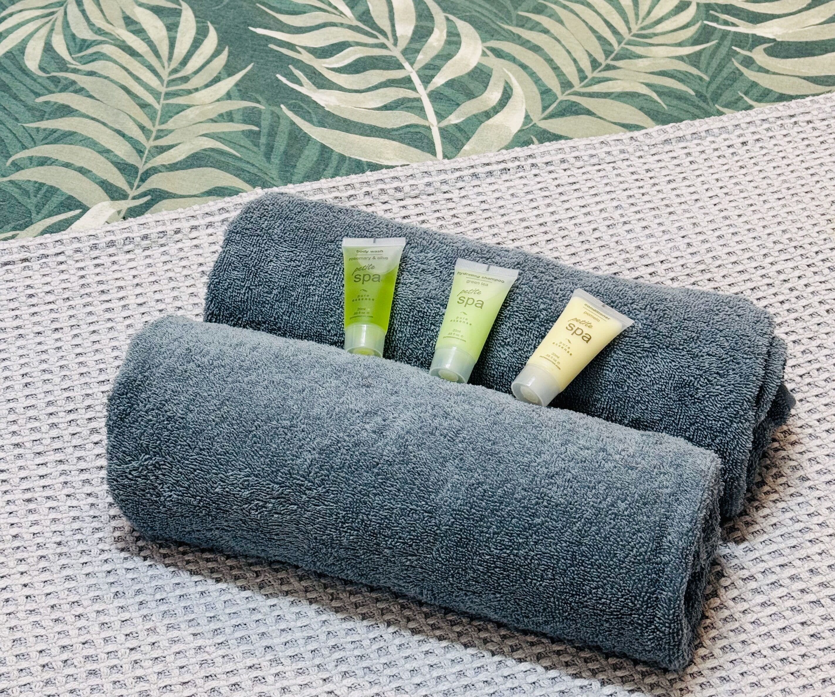 Una toalla enrollada con tres productos de spa sobre una superficie texturizada.