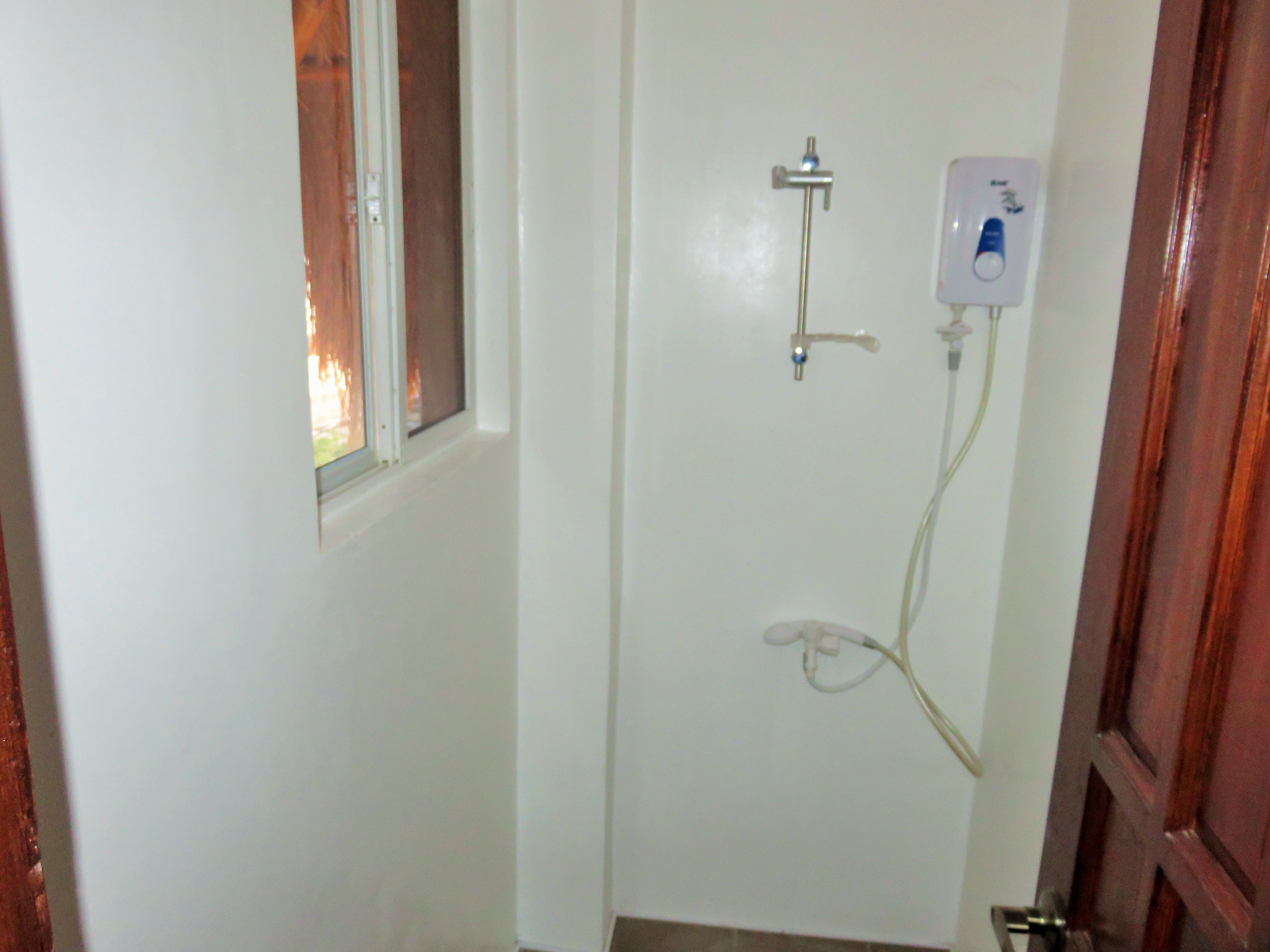 Un baño pequeño y blanco con ducha, una ventana y una puerta.