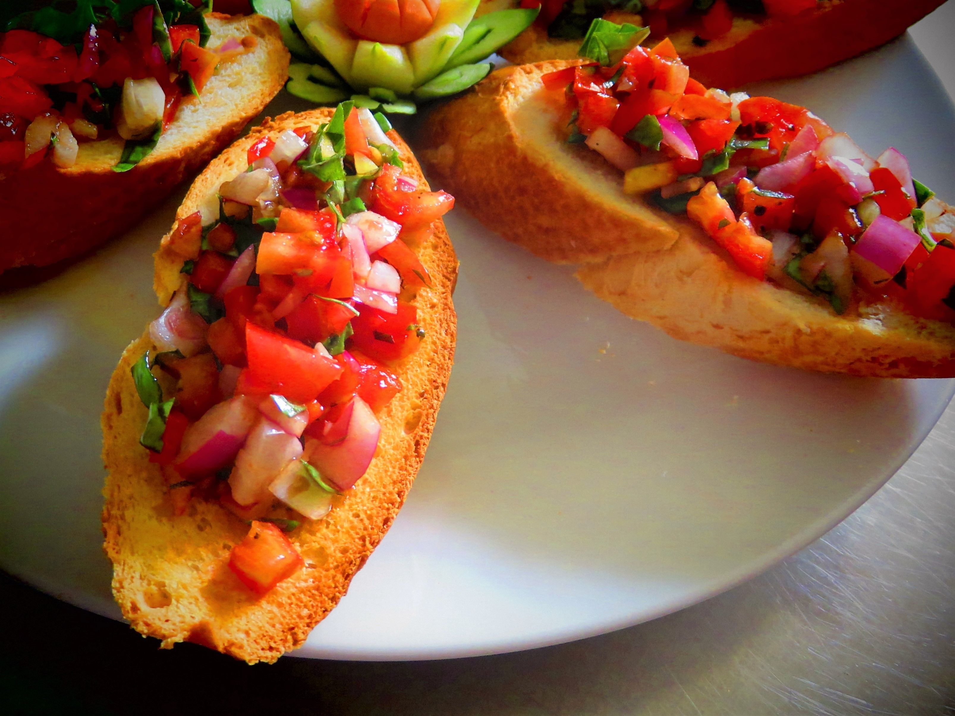 Une assiette contenant trois tranches de bruschetta garnies de tomates, d’oignons et d’herbes, le tout coupé en dés.