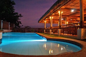 A swimming pool with a thatched-roof structure and columns, surrounded by a wooden fence. - Kav's Beach Resort (Zamboanguita)