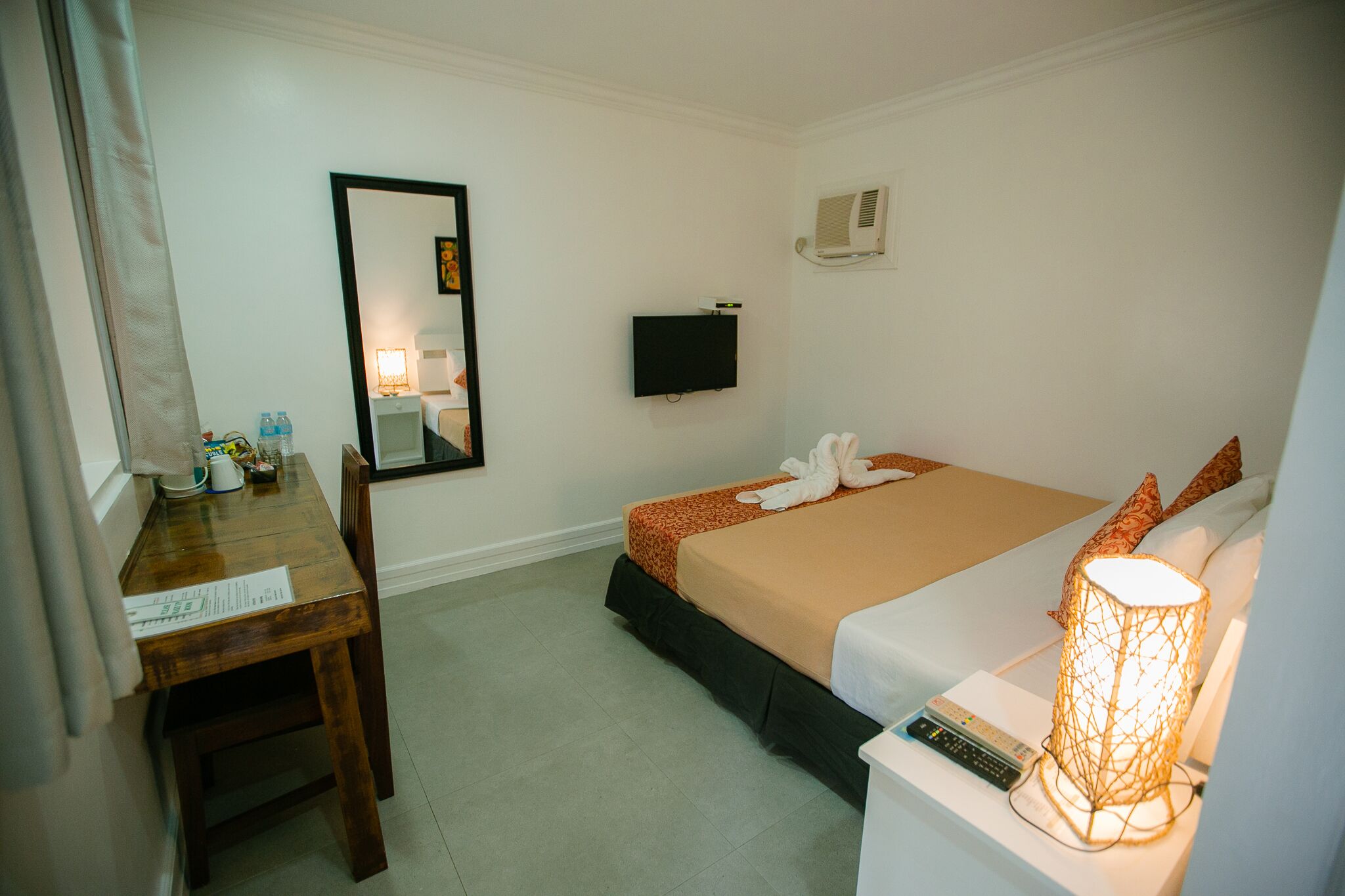 Une chambre d’hôtel équipée d’un lit, d’un bureau, d’une chaise, d’une télévision, d’une lampe et d’un miroir.