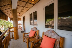 A wooden deck with a thatched roof, wooden chairs with orange cushions, and a view of greenery and rocks. - Kav's Beach Resort (Zamboanguita)