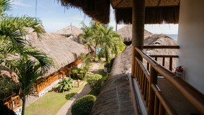 A resort with thatched-roof buildings, a balcony with a railing, and a view of the ocean. - Kav's Beach Resort (Zamboanguita)
