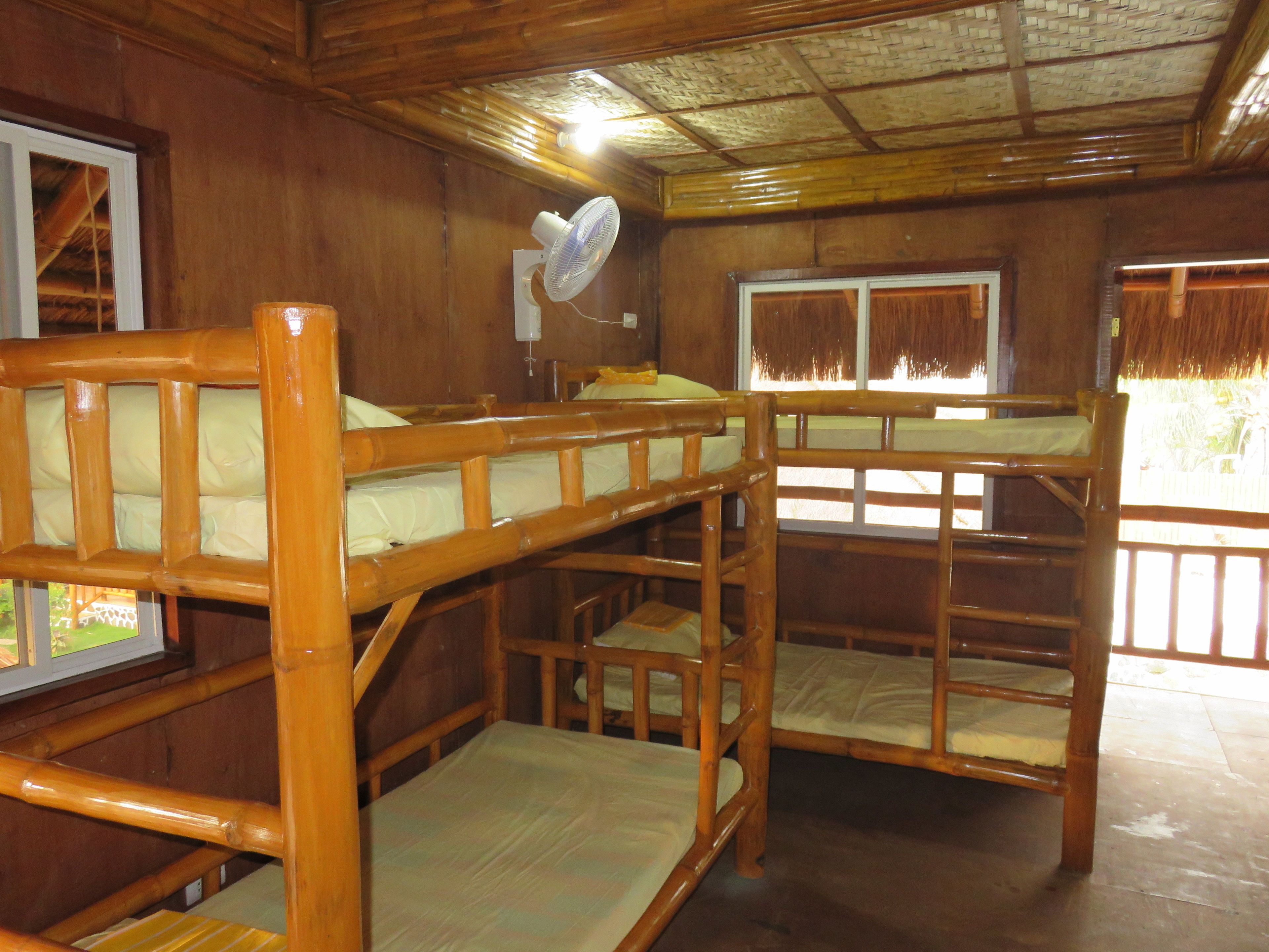 A wooden cabin with bunk beds, a fan, and windows.