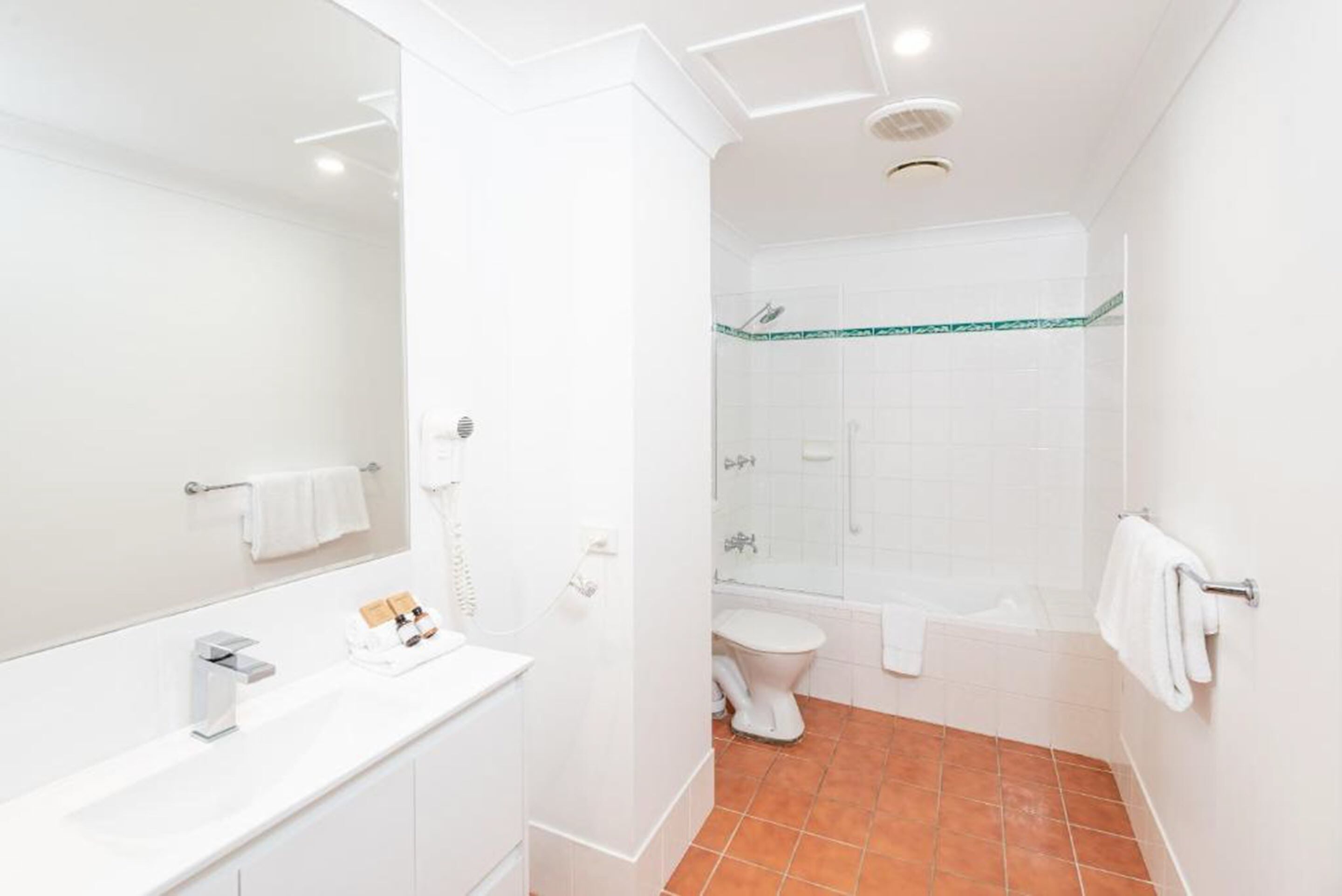 A modern bathroom with a white vanity, a large mirror, a toilet, and a shower area.