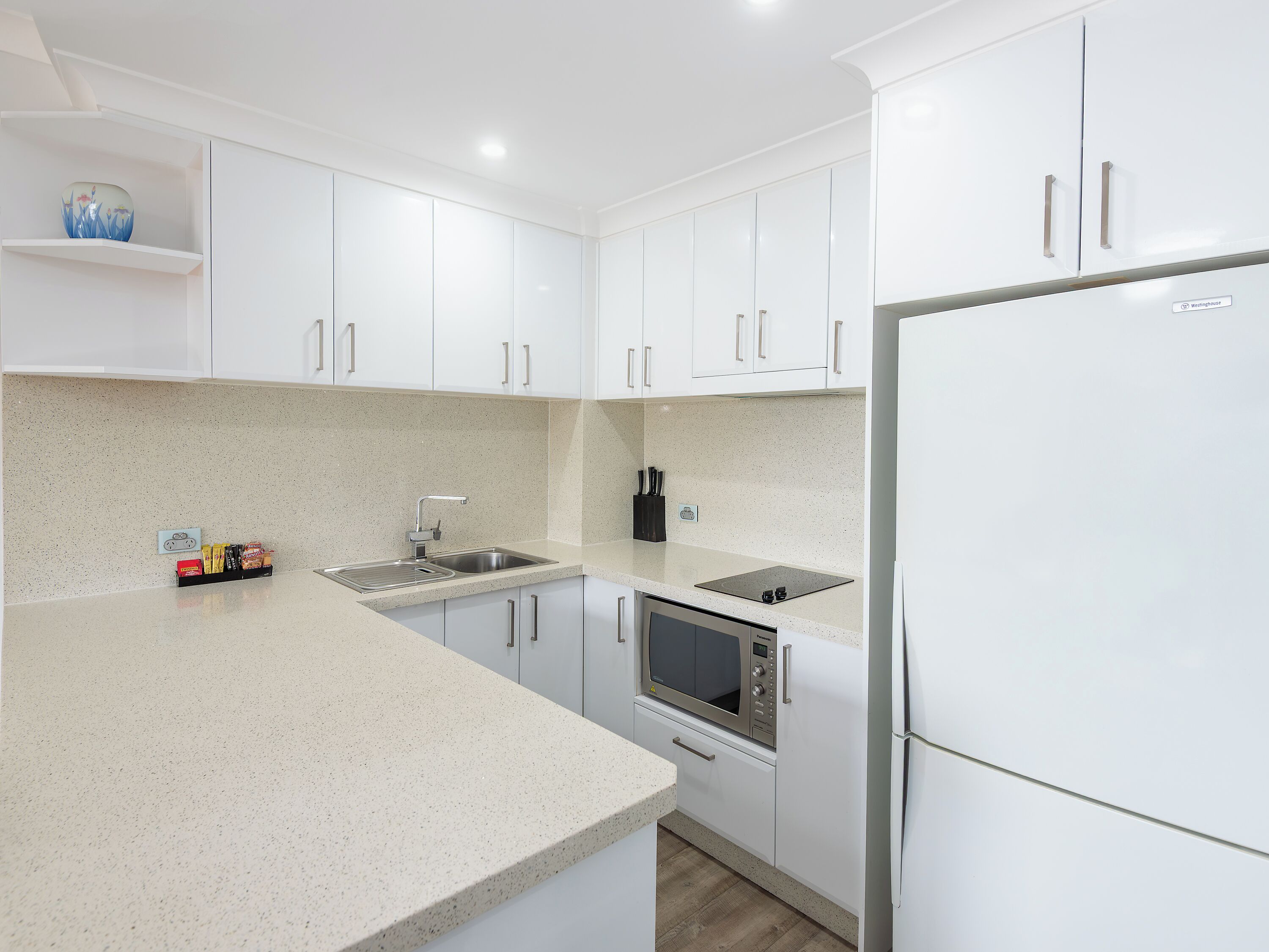 A modern kitchen with white cabinets, a stainless steel sink, a microwave, and a refrigerator.