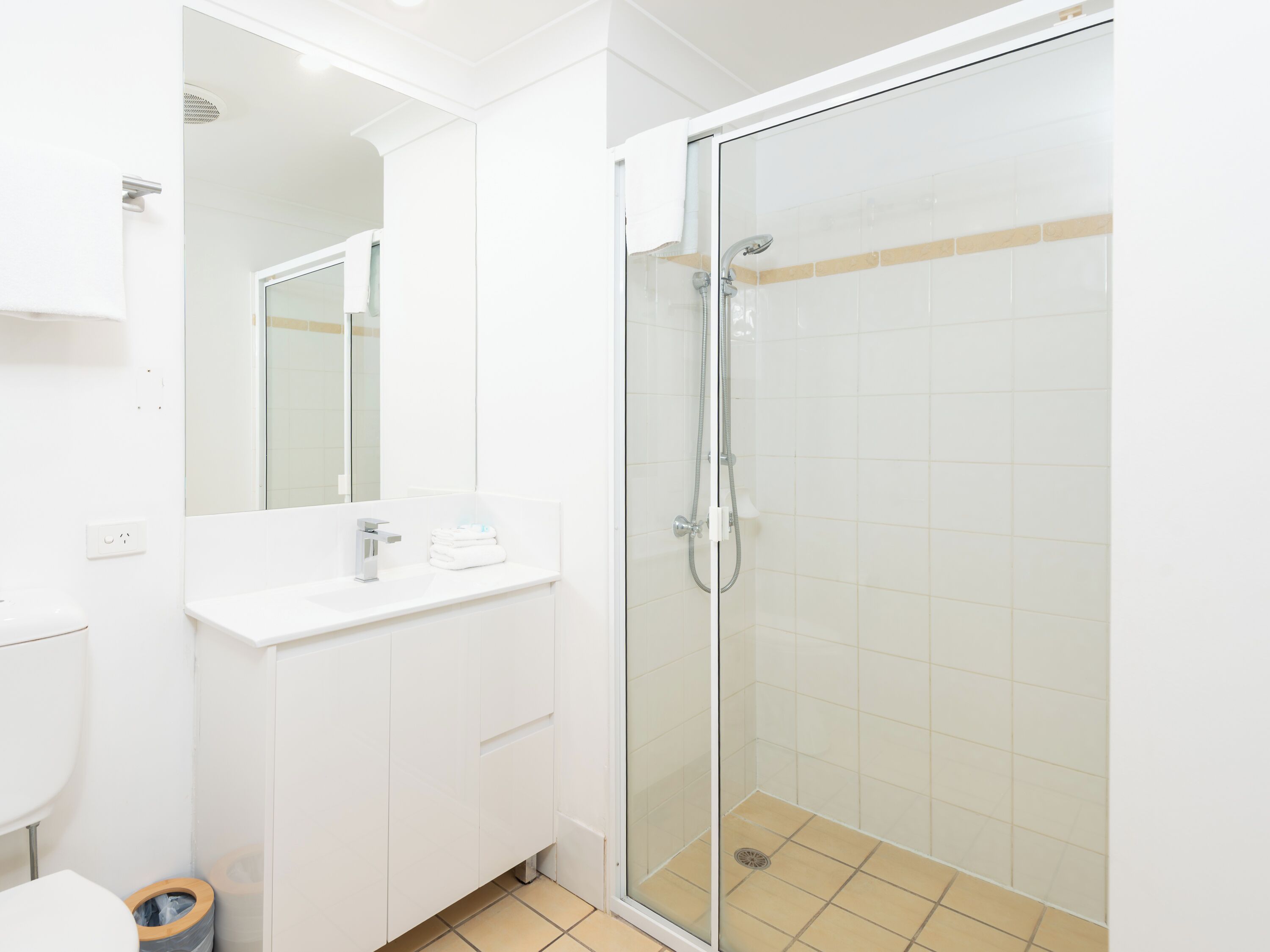 A modern bathroom with a glass-enclosed shower, white cabinetry, and a mirror above the sink.