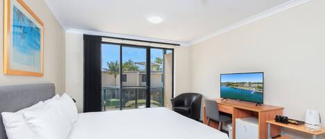 A hotel room with a bed, a desk, a television, and a view of a coastal area.