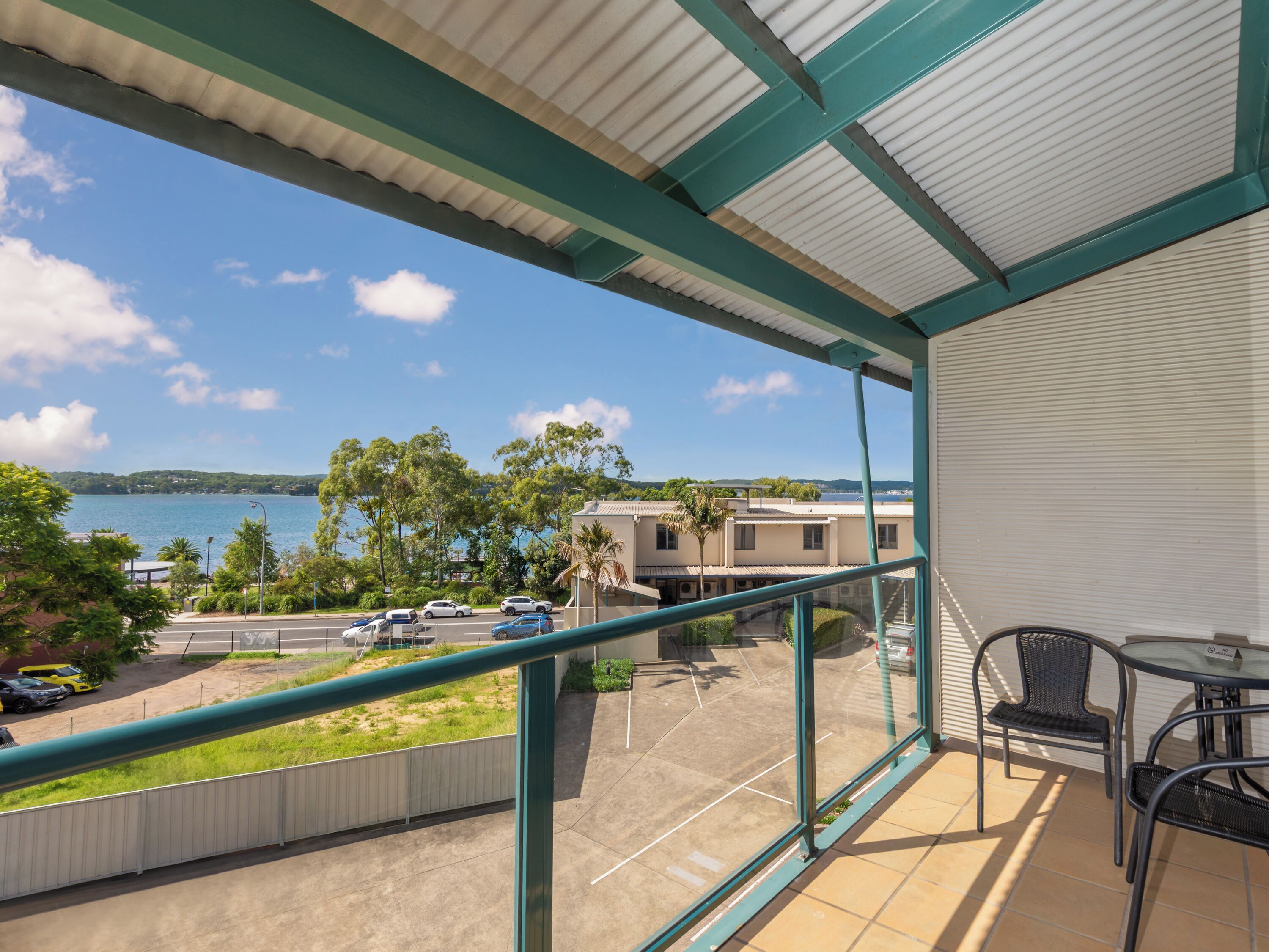 A balcony with a view of a parking lot, a body of water, and buildings in the distance.