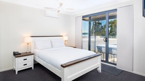 A bedroom with a bed, bedside tables, a lamp, and a view through a sliding glass door.