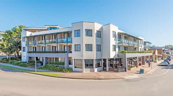 Un hotel moderno de varios pisos, con balcones, asientos exteriores y vista a la calle.