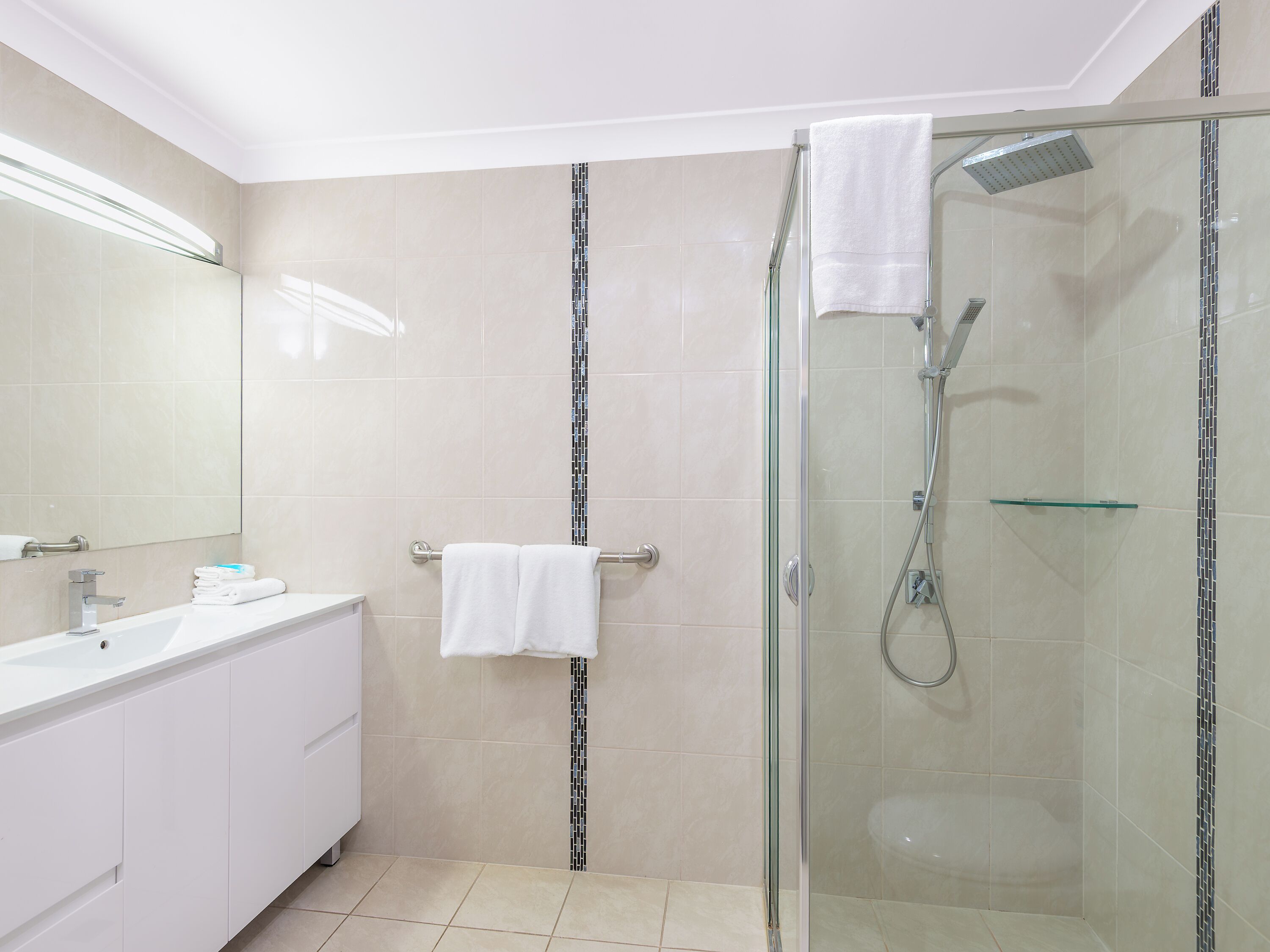 A modern bathroom with a glass-enclosed shower, a white vanity with a mirror, and a tiled floor.