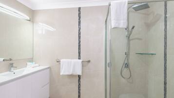 A modern bathroom with a glass-enclosed shower, a white vanity with a mirror, and a tiled floor.